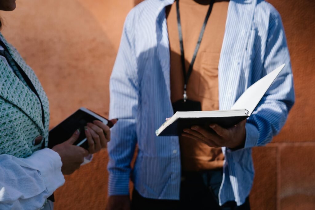 Close-up of two adults holding and discussing books under sunlight outdoors.